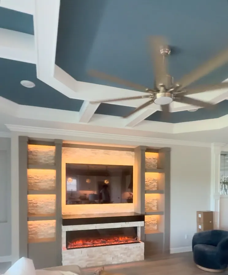 Coffered ceiling and a stone fireplace media wall with lit shelves