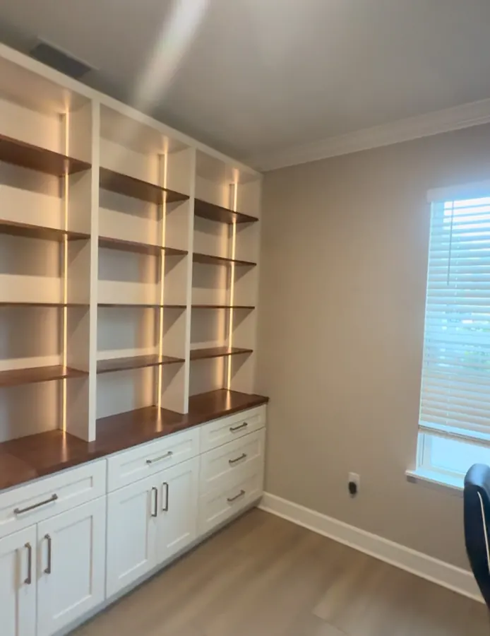 Office built-ins with lit wood shelves and white cabinets