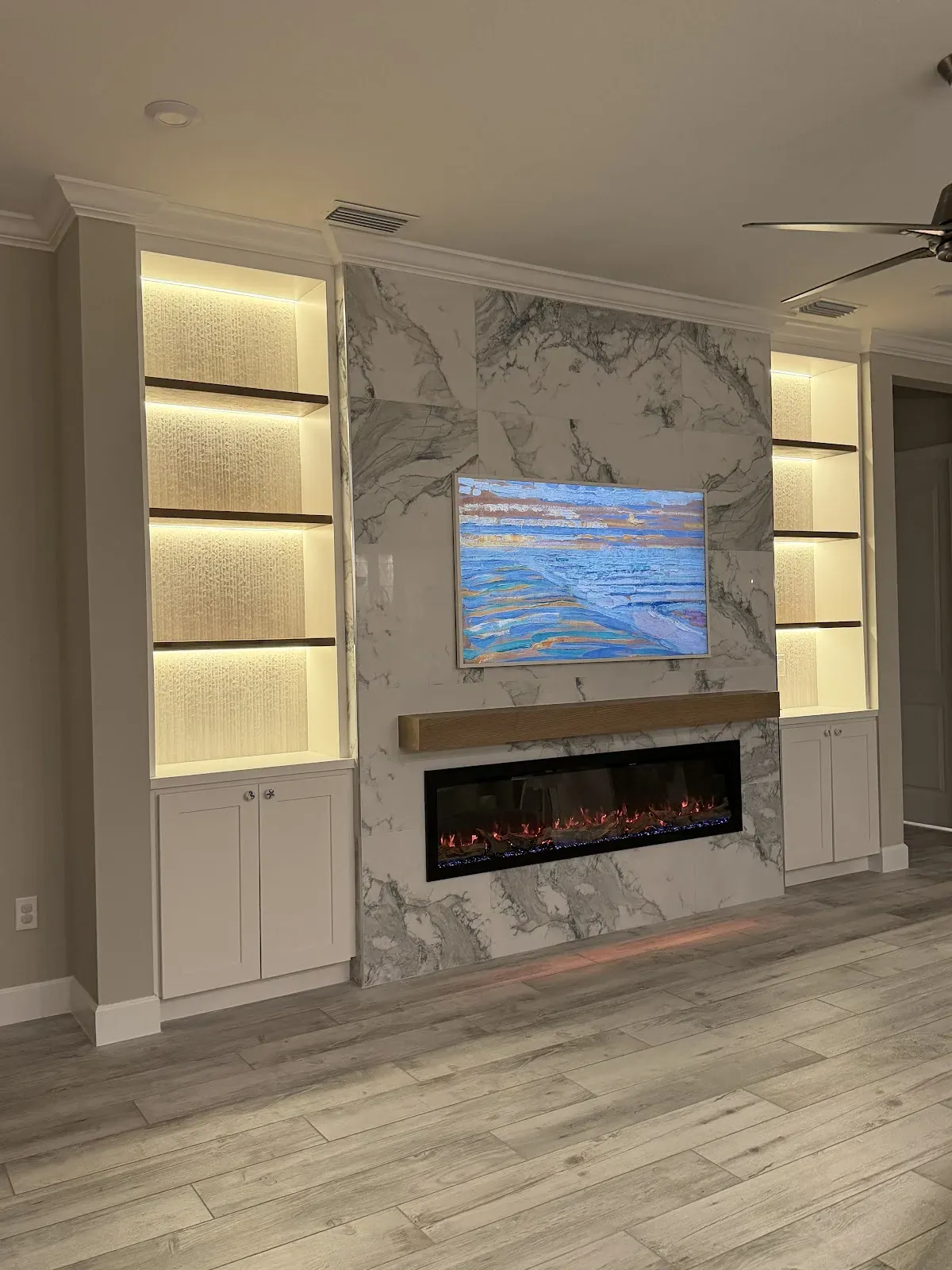 Marble fireplace wall with lit built-in shelving by JJ Nexus